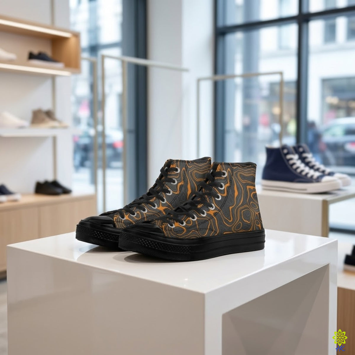 A pair of high-top sneakers displayed on a white pedestal inside a modern shoe store. The sneakers feature a black base with a brown and orange topographic contour pattern on the sides, black laces, and black soles.