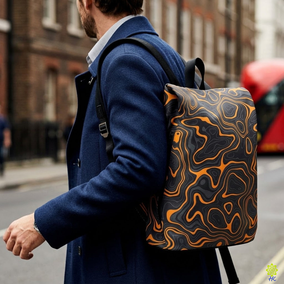 A man in a navy blue coat carrying a black backpack with an orange and gray wavy topographic pattern, photographed on a city street.