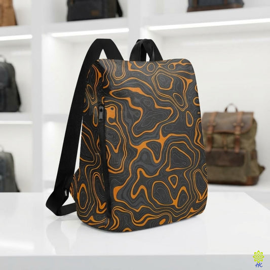 A backpack with a black and orange topographic contour pattern, displayed on a white table with blurred shelves of other bags in the background.