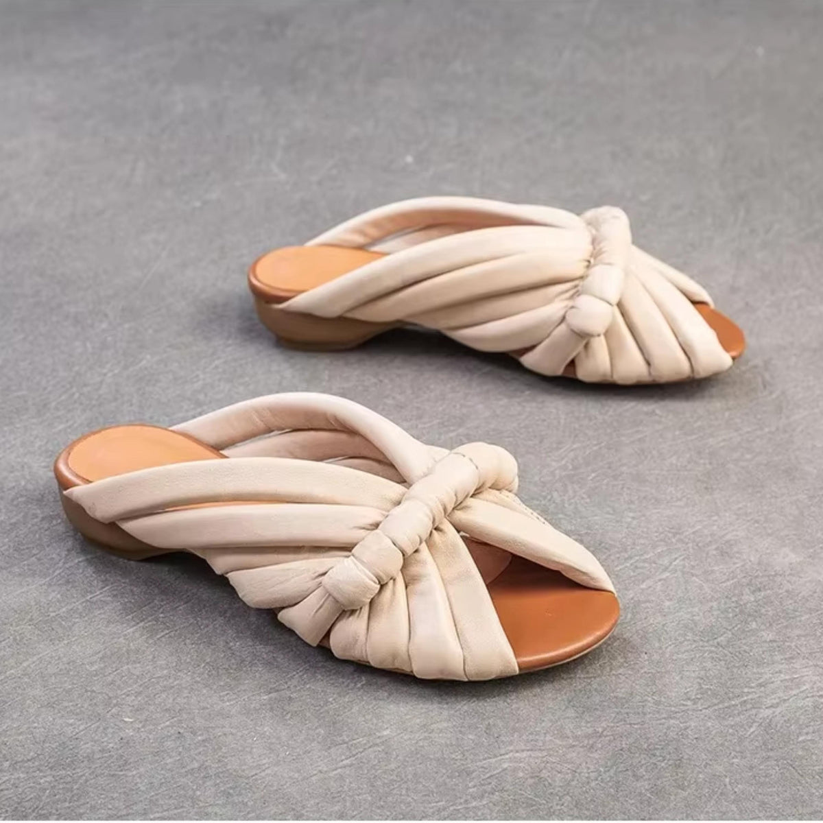 A pair of beige knotted sandals on a gray surface.