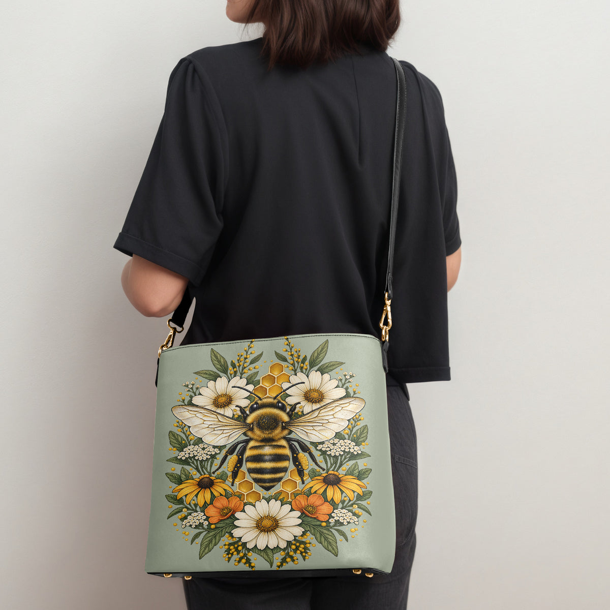 Sac porté épaule abeille posé au sol à côté d'un ordinateur portable, d'un téléphone, d'un portefeuille et d'une bouteille