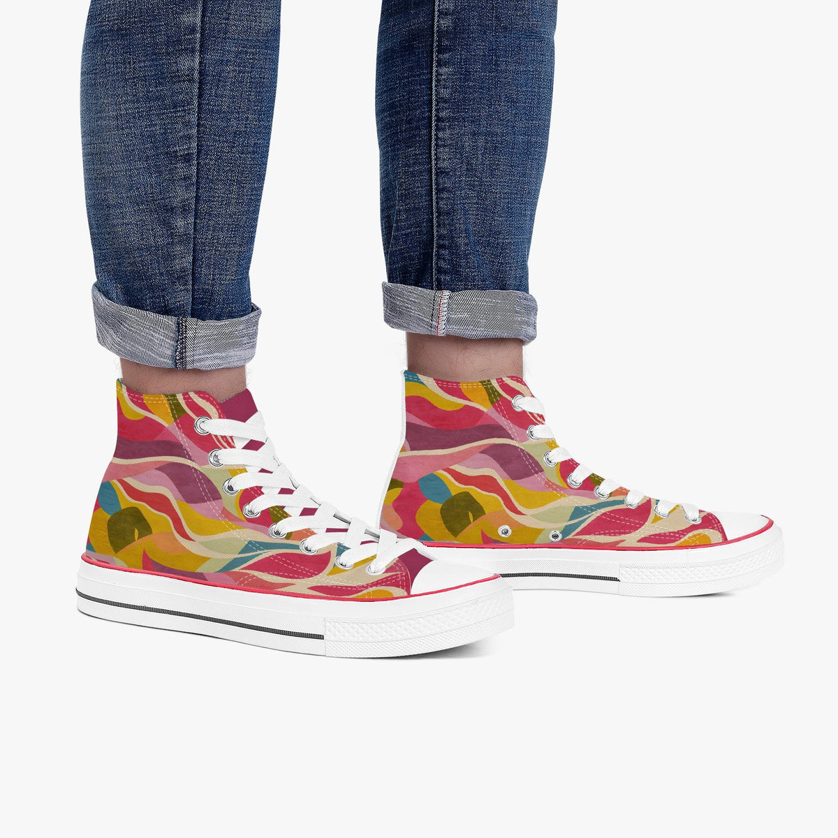 A pair of high-top canvas sneakers with a vibrant multicolor abstract pattern in pink, yellow, orange, and green, worn with cuffed blue jeans against a plain white background.