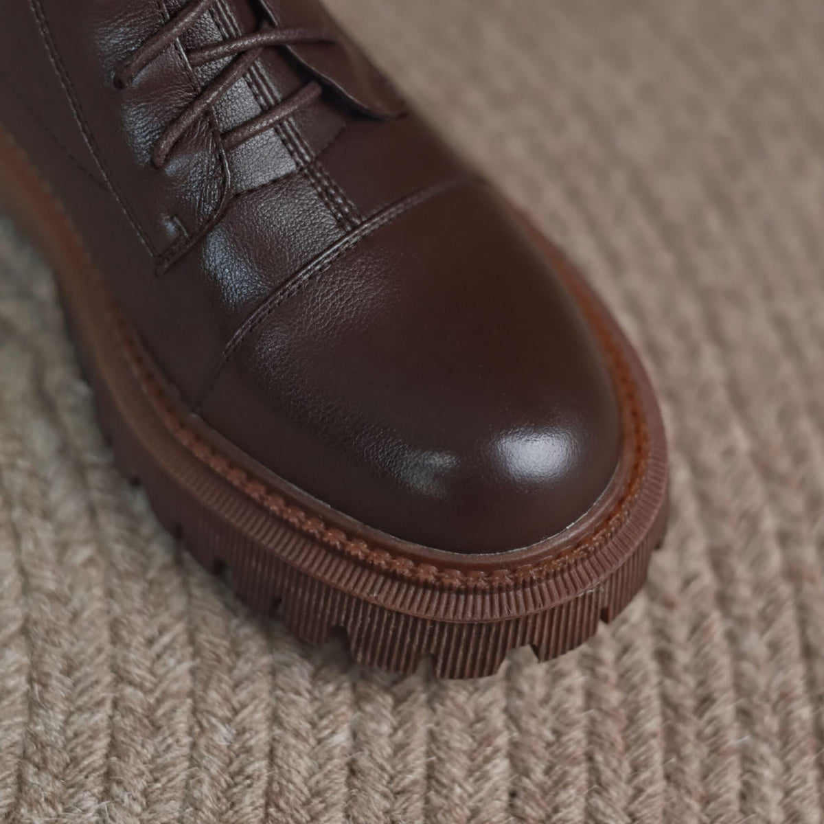 A close-up view of a brown leather shoe with a thick sole and laces, resting on a textured surface.