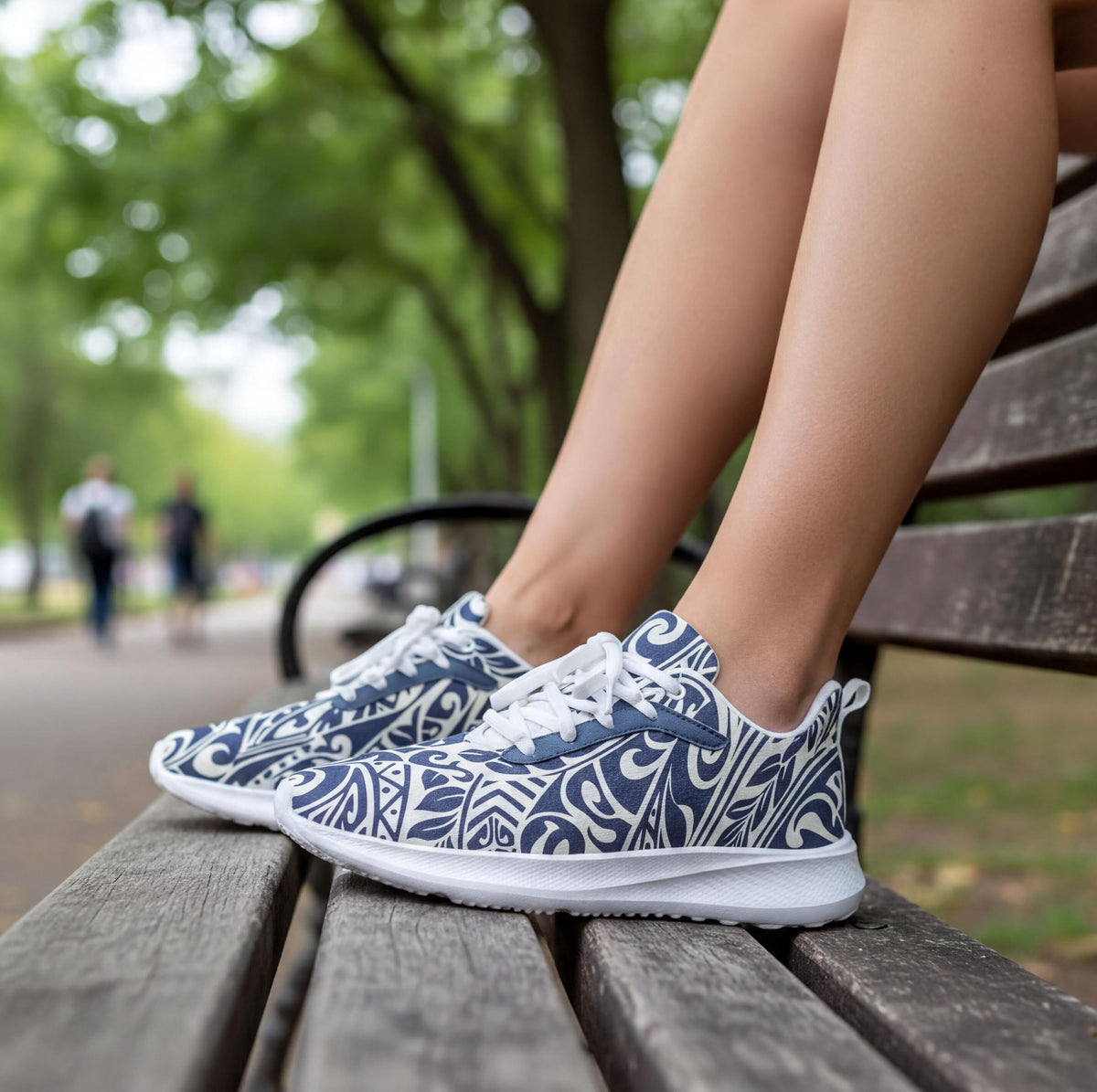 A pair of blue and white patterned sneakers is placed on a wooden bench in a park setting.