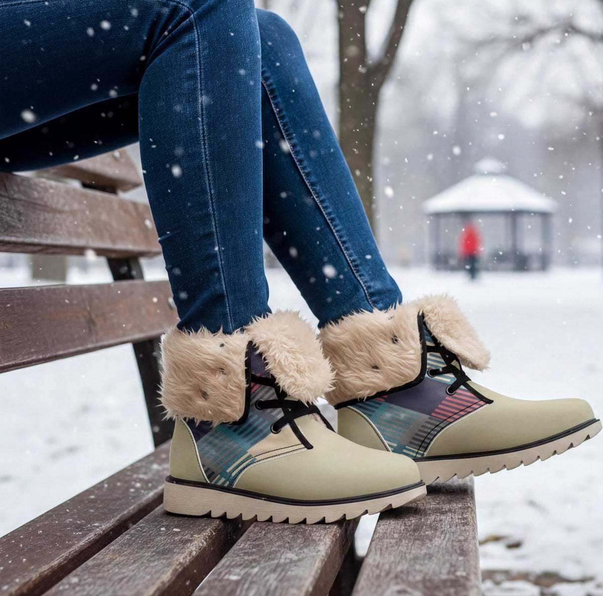 A person wearing blue jeans and tan boots sits on a wooden bench in a snowy park, with a gazebo visible in the background.
