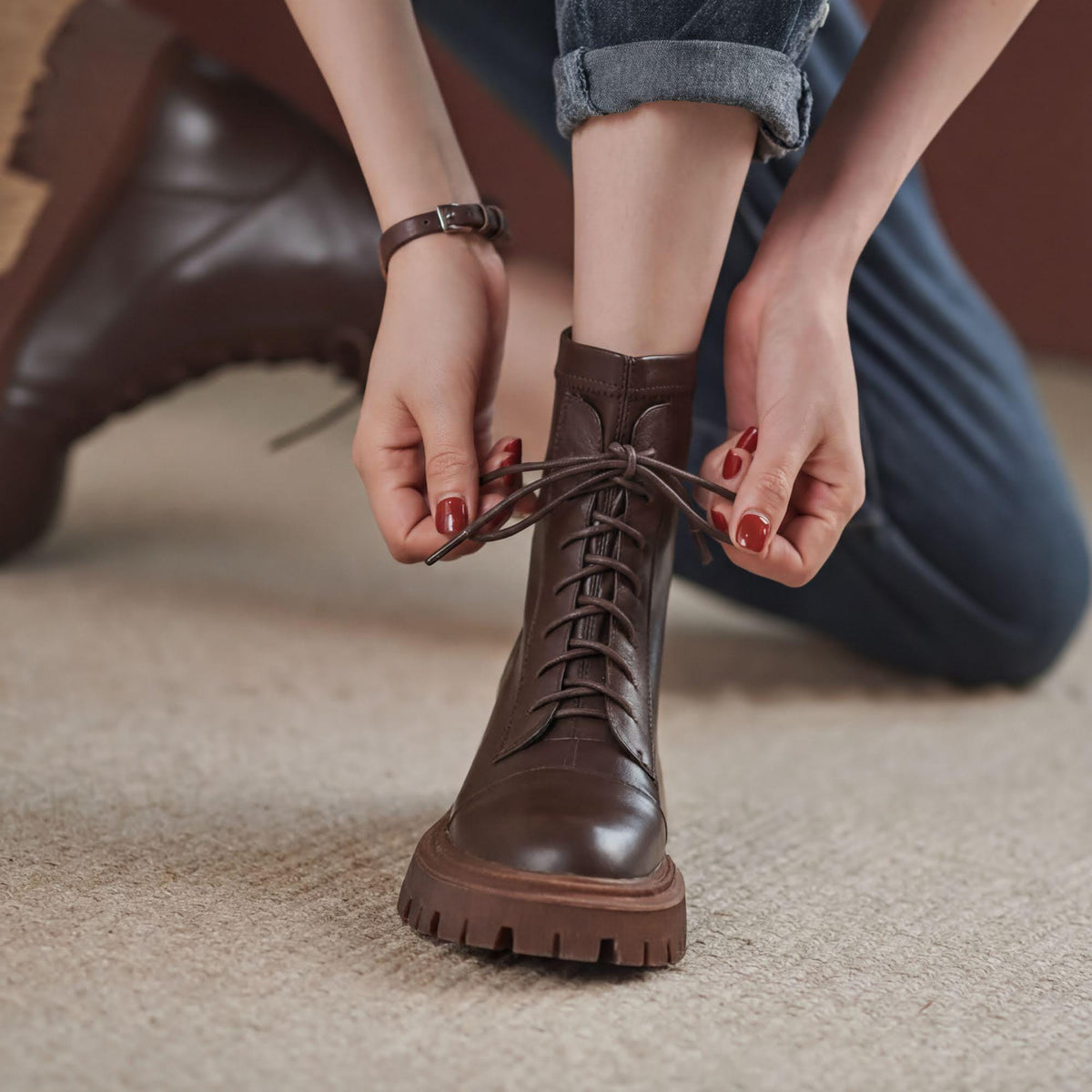 A person's feet wearing brown leather boots, with their hands tying the laces.