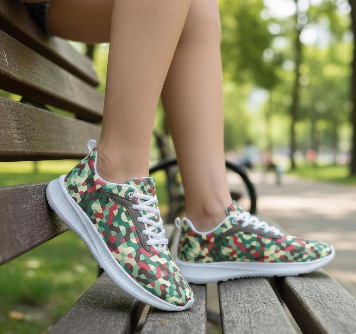 A person's feet wearing camouflage-patterned sneakers are resting on a wooden bench in a park setting.