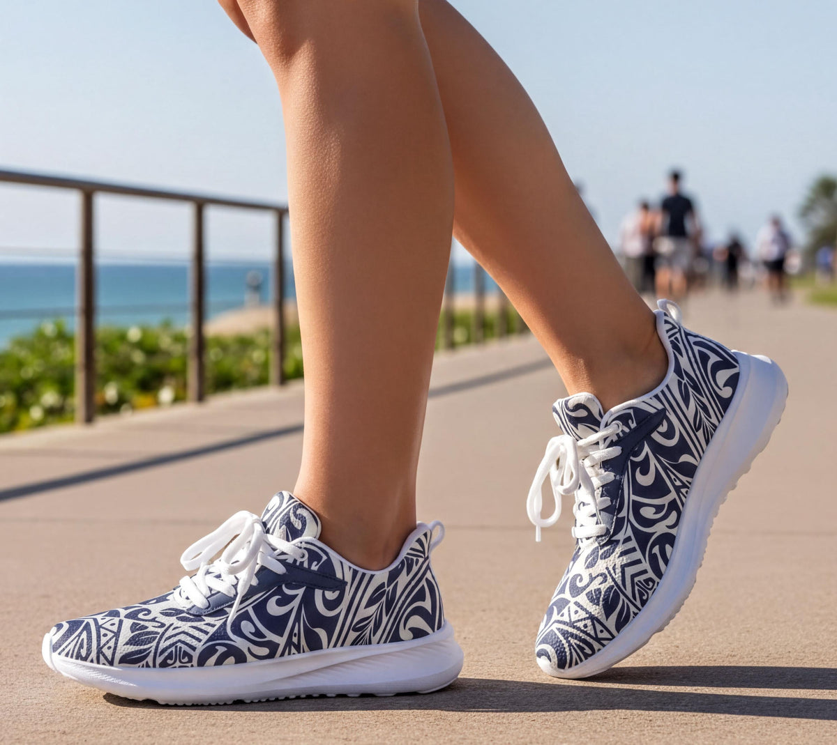 A person's feet wearing patterned sneakers, walking on a path near the ocean.
