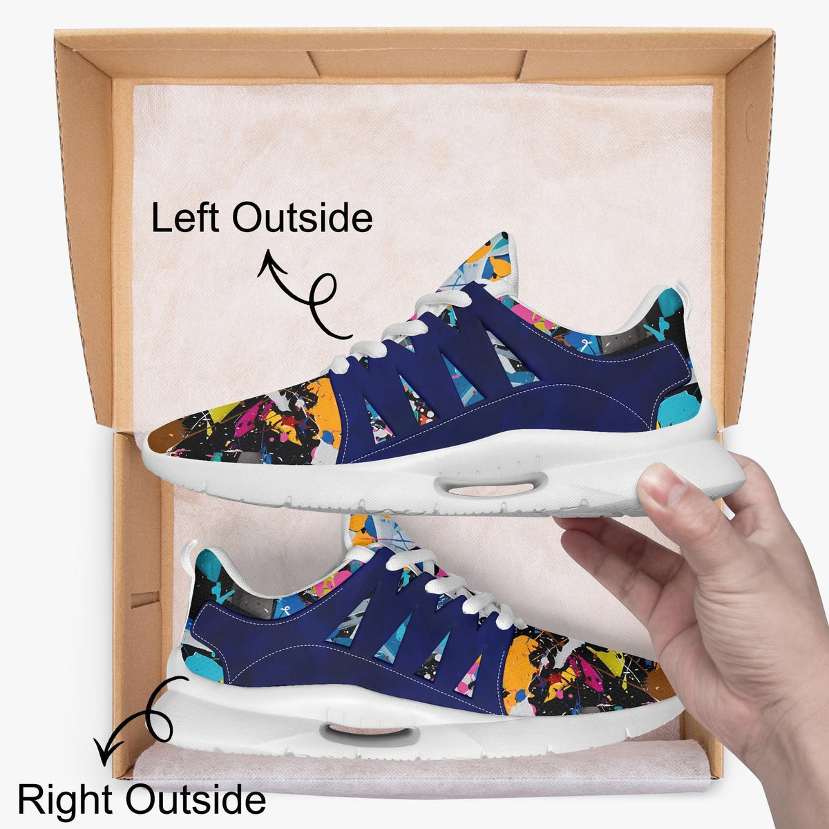 A hand is holding a pair of colorful sneakers with a patterned design, standing inside a cardboard box.