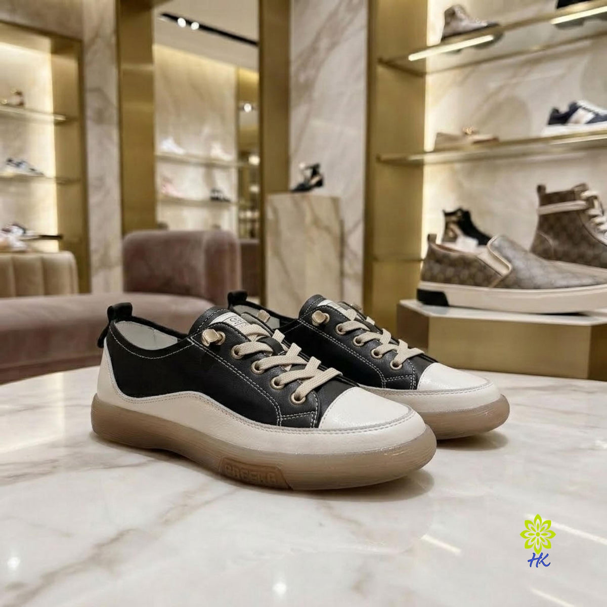 A pair of black and off-white low-top sneakers with beige laces and gum soles, displayed on a marble counter inside a luxury shoe boutique.