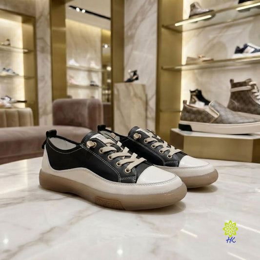 A pair of black and off-white low-top sneakers with beige laces and gum soles, displayed on a marble counter inside a luxury shoe boutique.