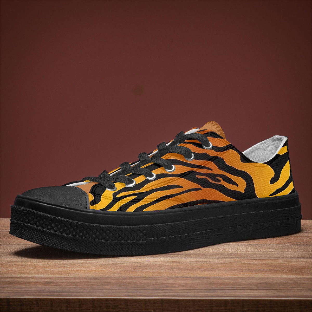 A pair of black and orange tiger-striped sneakers is displayed on a wooden surface against a red background.