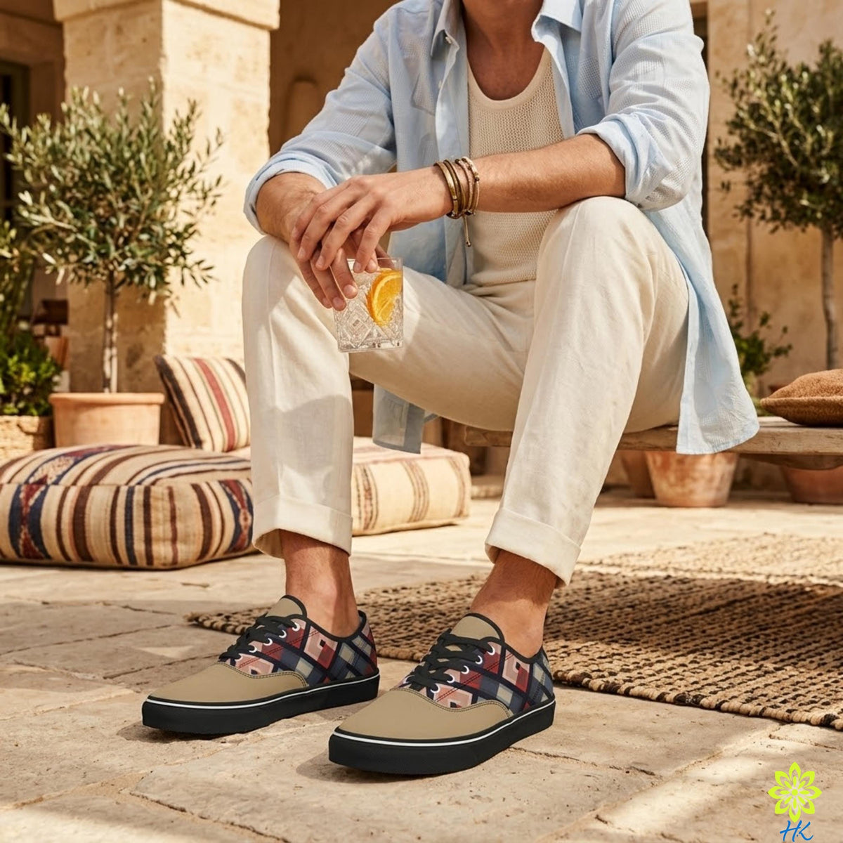 A man is sitting on a bench, wearing a blue shirt, white pants, and patterned shoes, holding a drink in his hand.