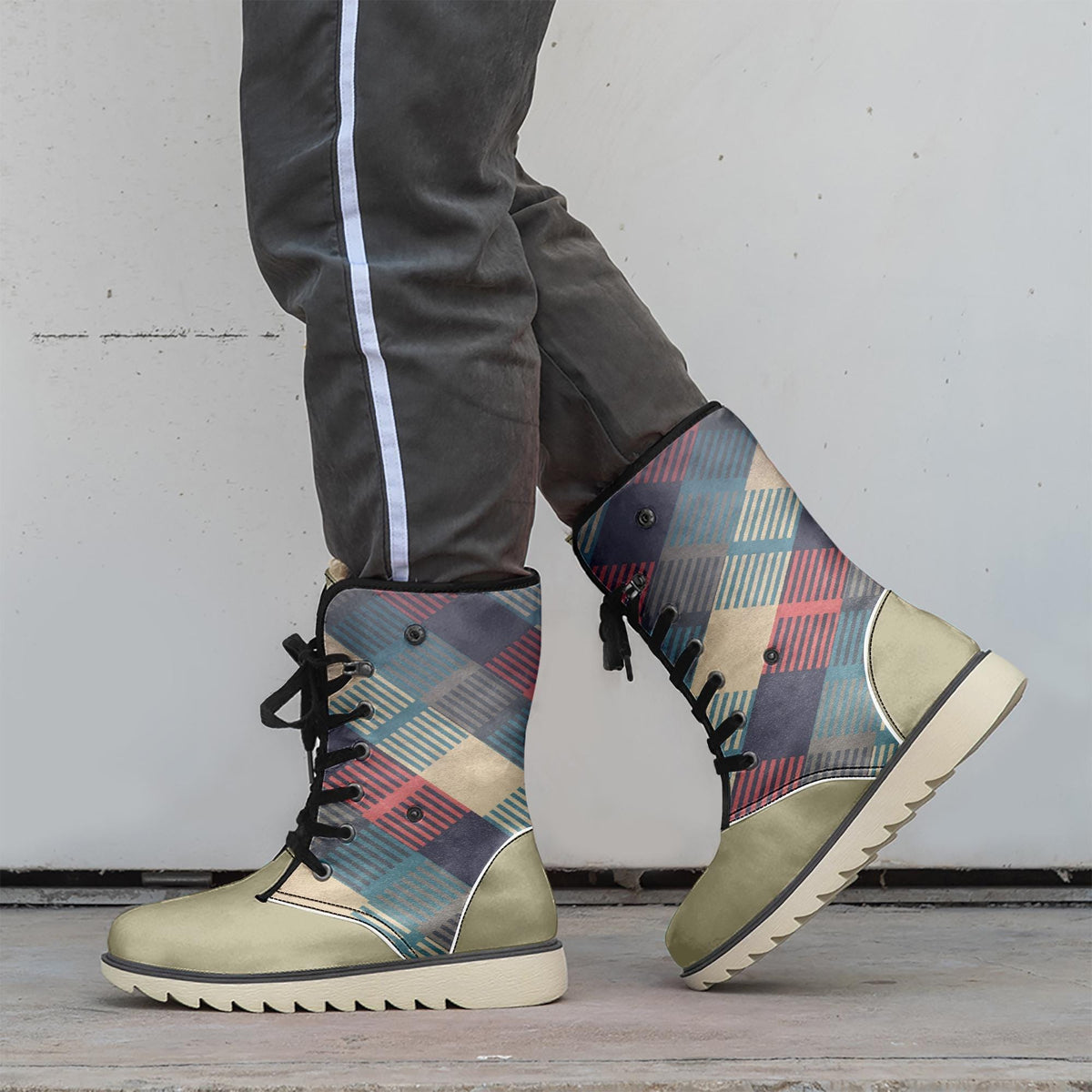 A person wearing a pair of colorful plaid patterned boots stands against a white wall.