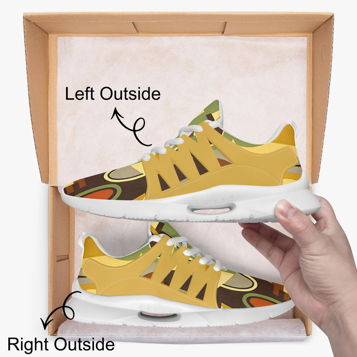 A hand is holding a pair of yellow and brown patterned sneakers, with the left shoe positioned outside the box and the right shoe inside the box.