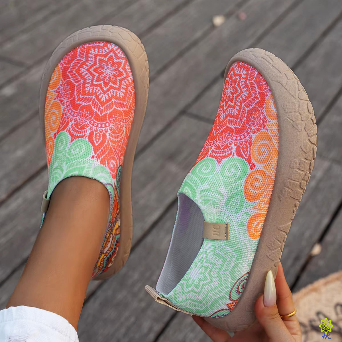 Primo piano di scarpe slip-on boho a mandala tenute in mano, con la stampa verde, arancione e rossa e la linguetta sul tallon