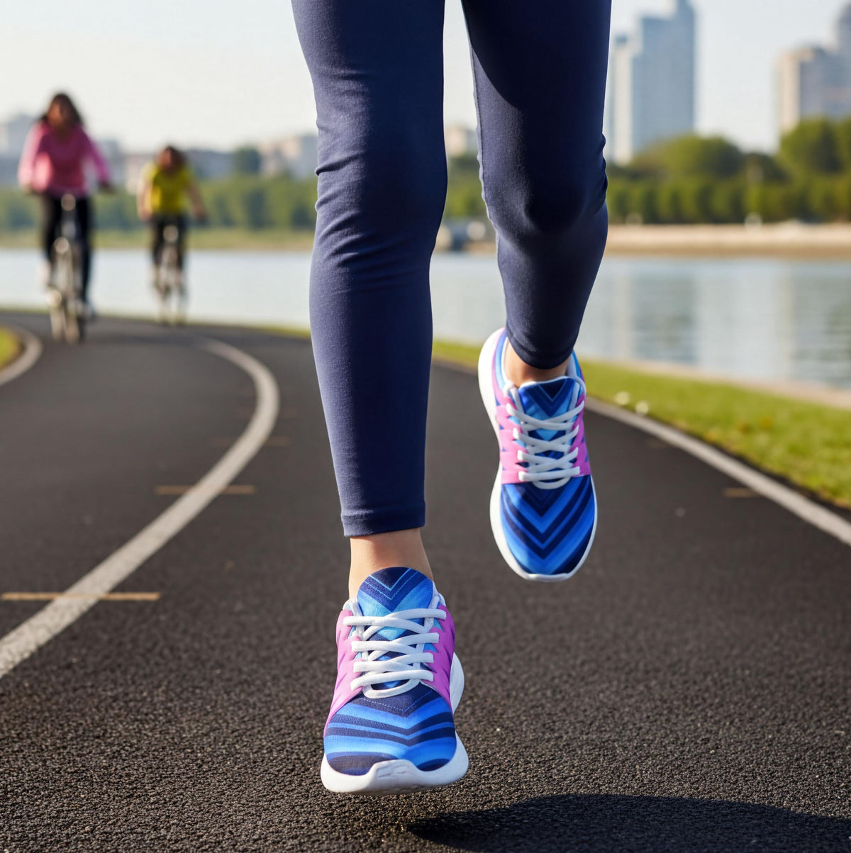 A person wearing blue leggings and pink and blue sneakers is running on a paved path, with another person riding a bicycle in the background.