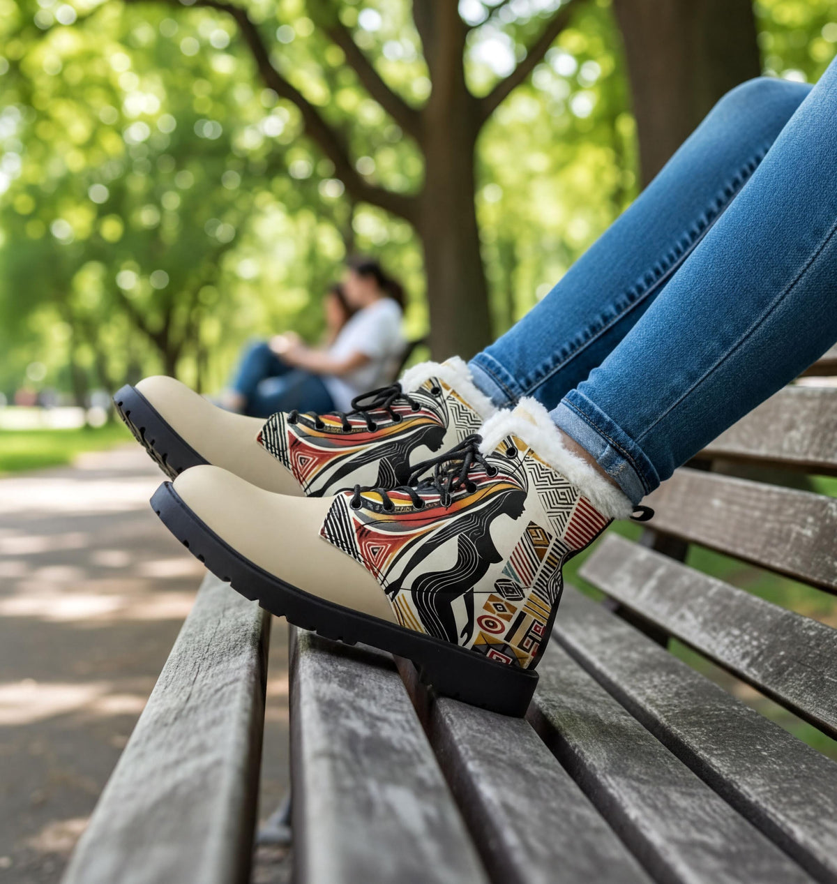 A person's feet wearing patterned boots are resting on a wooden bench in a park setting.