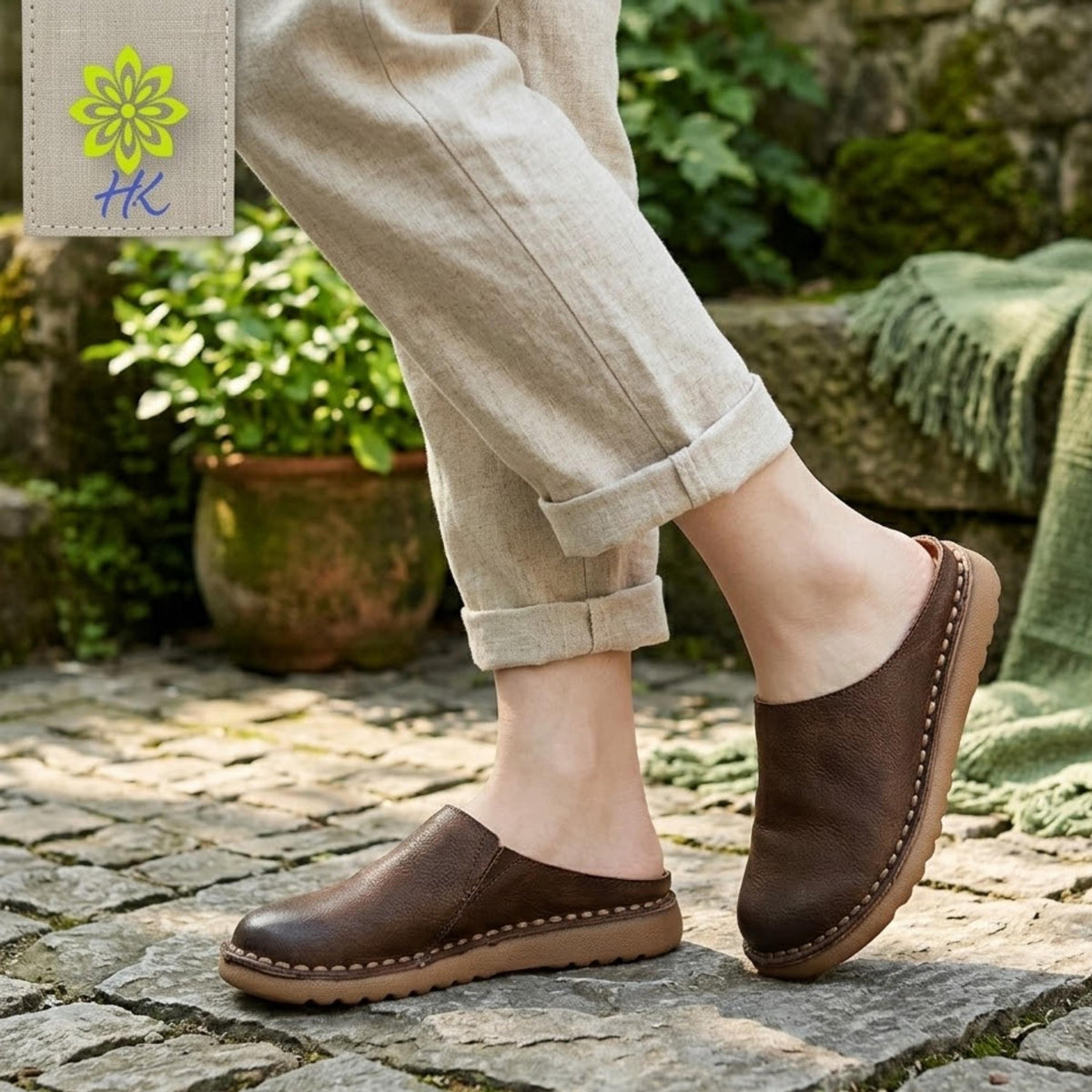 A person wearing beige pants and brown leather shoes is standing on a stone path in a garden setting.