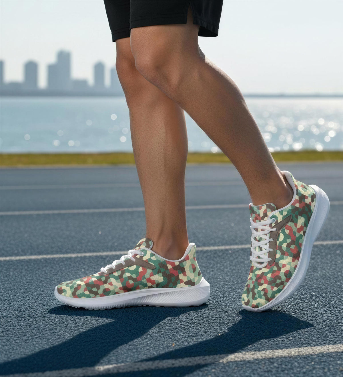 A person wearing camouflage-patterned running shoes is standing on a track near a body of water, with a city skyline visible in the background.