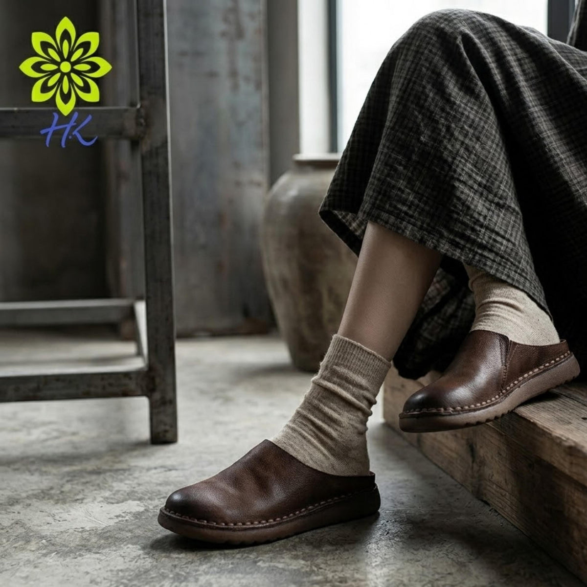 A person's legs wearing brown leather shoes and beige socks are shown in a close-up shot, with a wooden bench and a vase visible in the background.