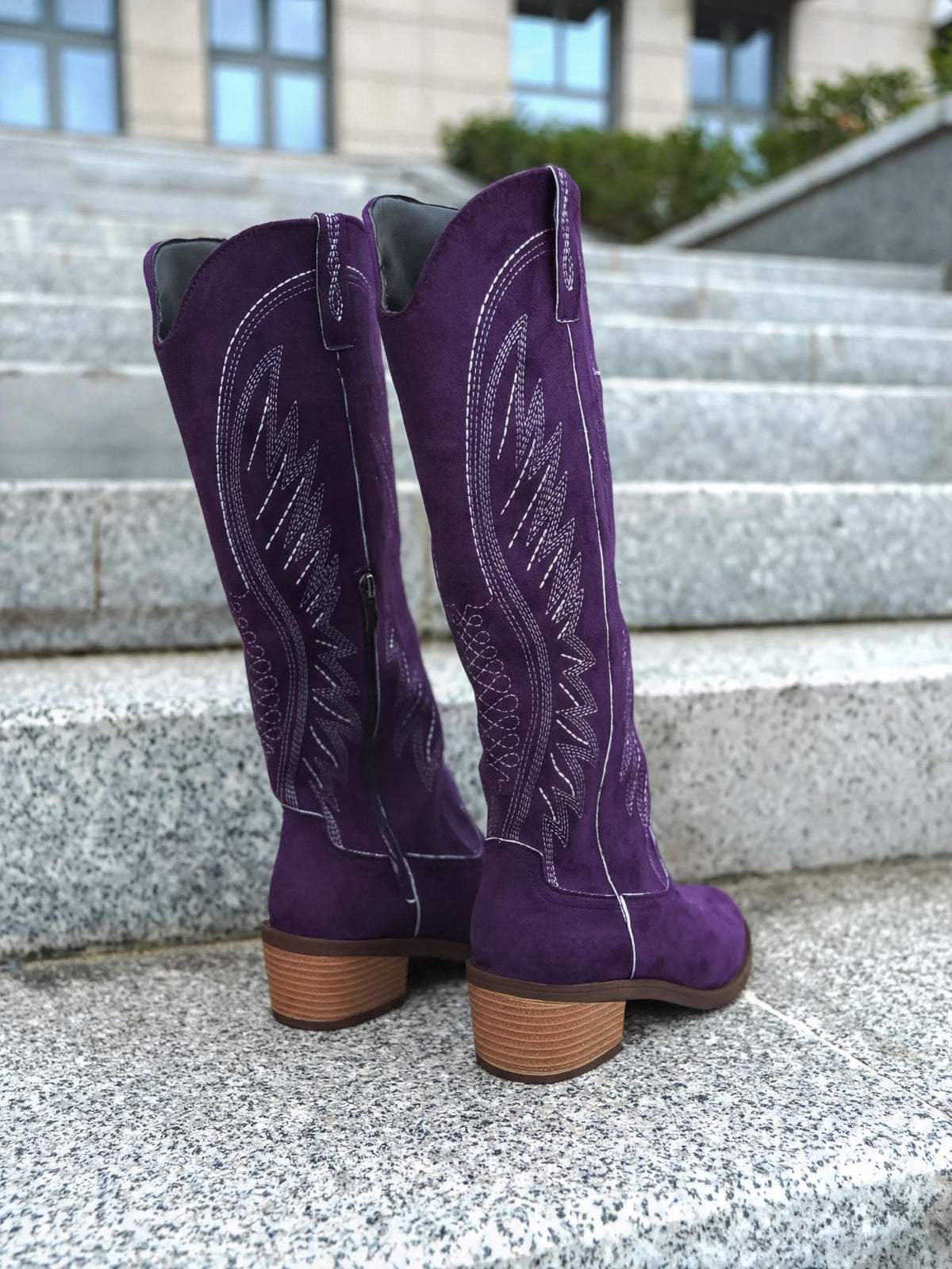 A pair of purple suede cowboy boots with decorative embroidery on the sides, standing on a set of stairs.