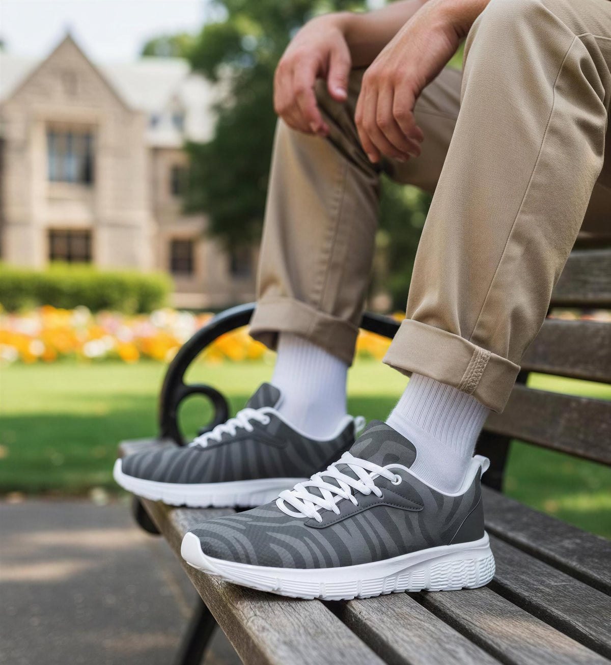 A person is sitting on a wooden bench in a park, wearing gray and white sneakers.