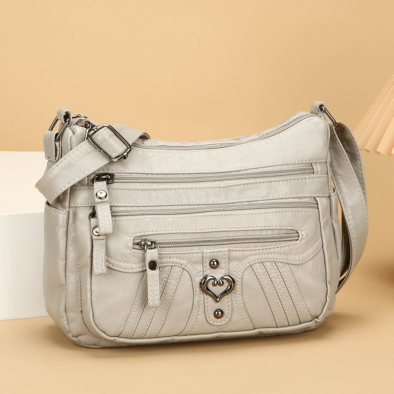 Multi-Pocket-Umhängetasche in Creme aus weichem PU-Kunstleder mit Herzakzent auf beigefarbenem Hintergrund