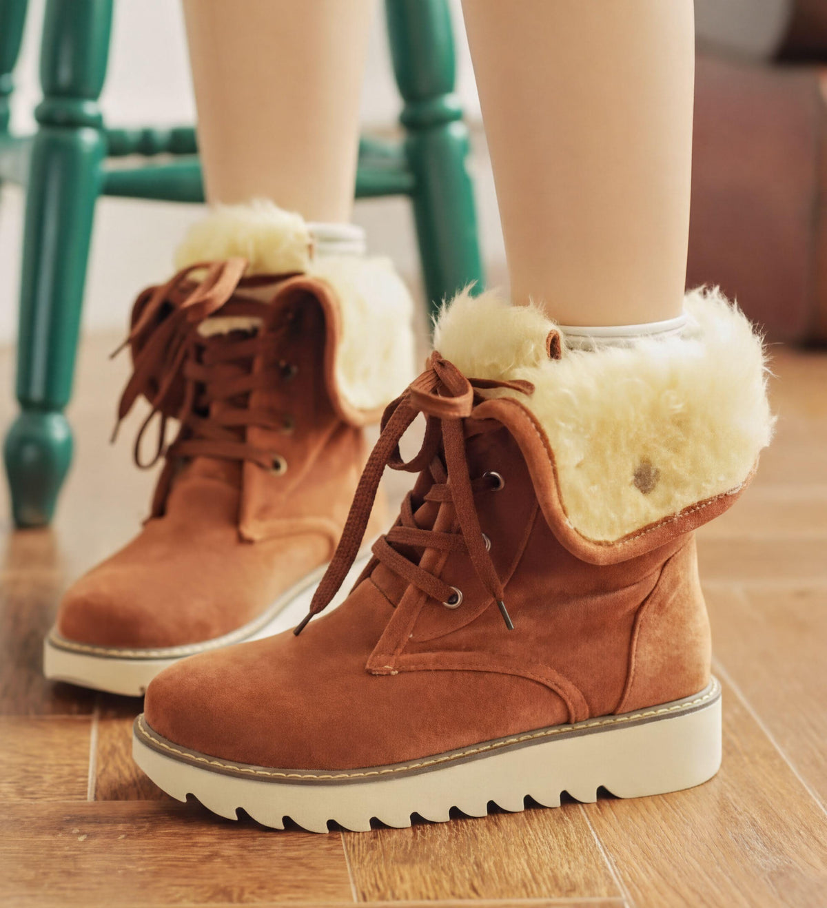 A pair of brown suede boots with white fur lining, worn by a person standing on a wooden floor.
