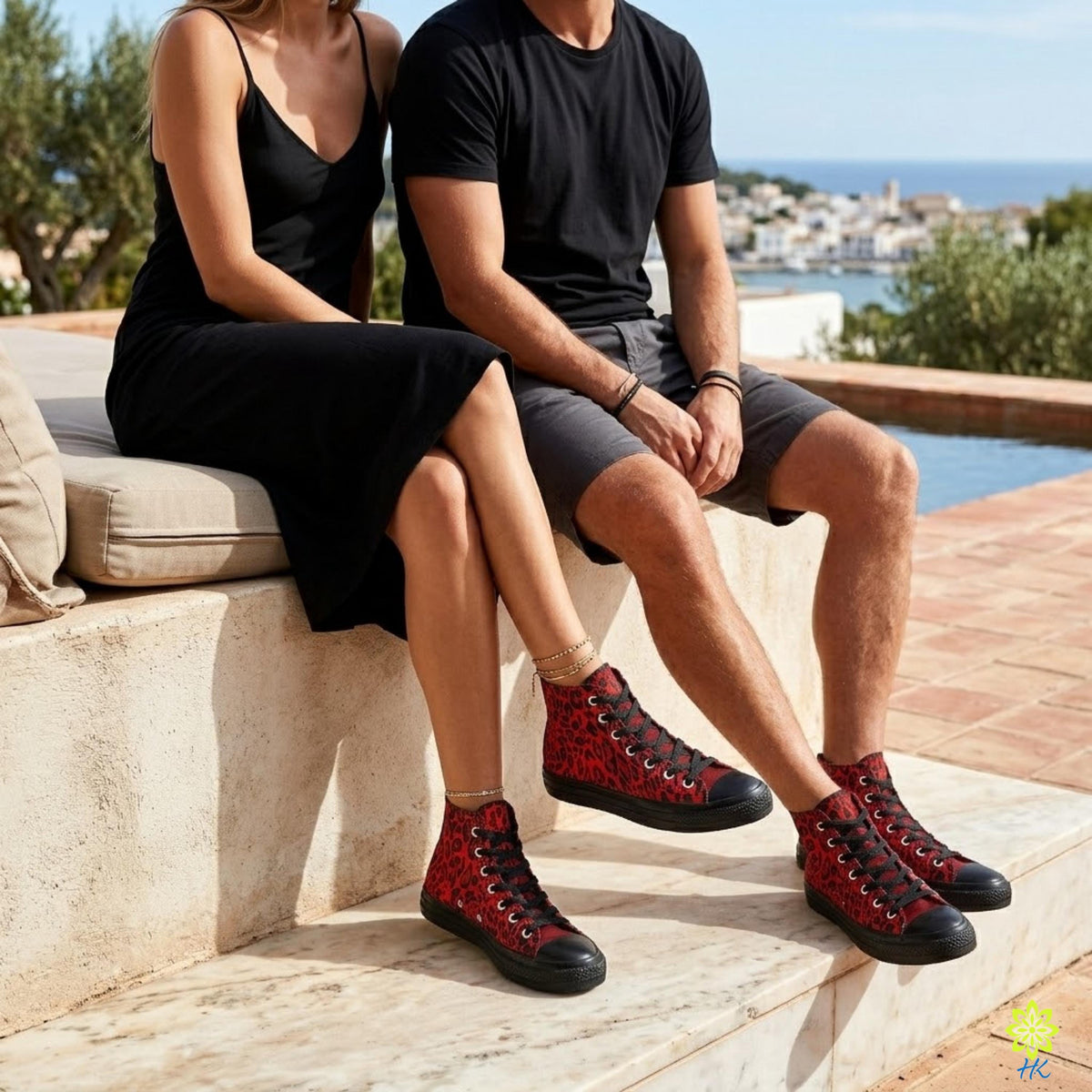 A man and a woman sitting on a stone bench, both wearing black clothing and red high-top sneakers.